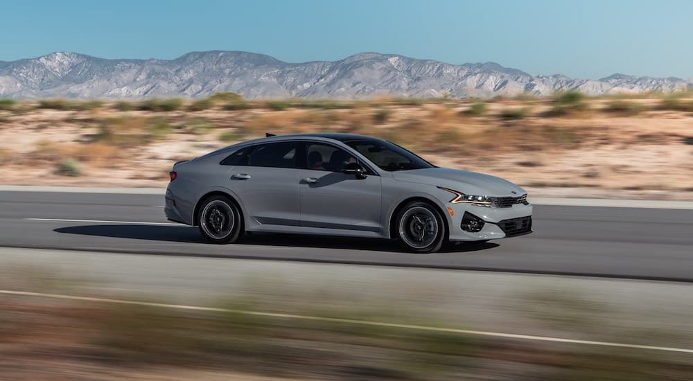 A grey 2021 Kia K5 GT is shown driving down the road after leaving a Kia dealership.
