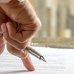 A hand holding a pen is reviewing Kia lease turn in paperwork.