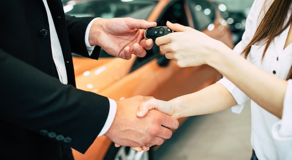 A salesman is shaking the hand of a woman and passing her a key.