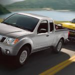 A silver 2019 Nissan Frontier is shown towing a car after leaving a used truck dealer.