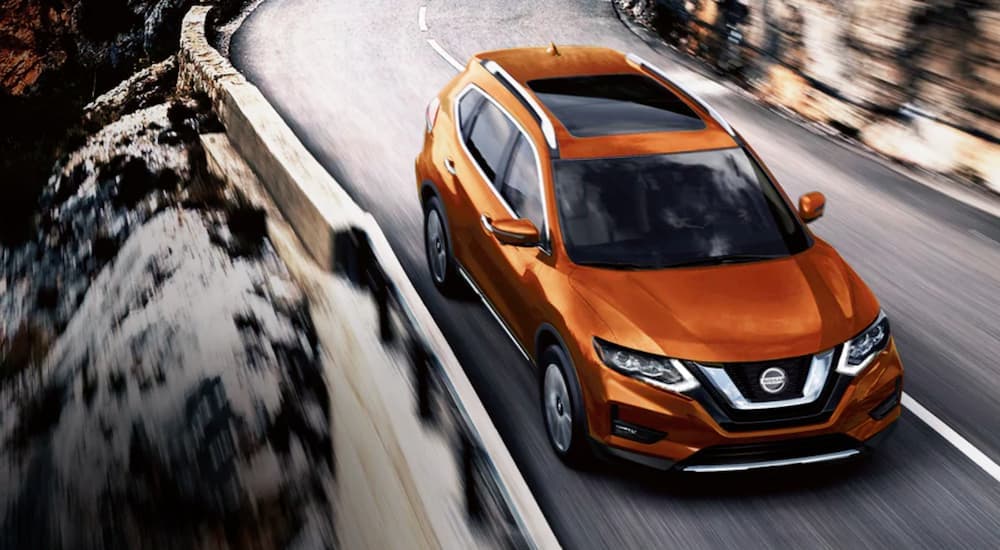 An orange 2020 Nissan Rogue is driving on an open road.