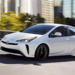 A white 2020 Toyota Prius is shown driving through a city.