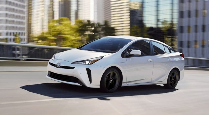 A white 2020 Toyota Prius is shown driving through a city.