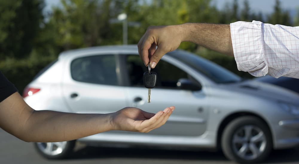A salesman is passing a set of keys to a customer at a used car lot.
