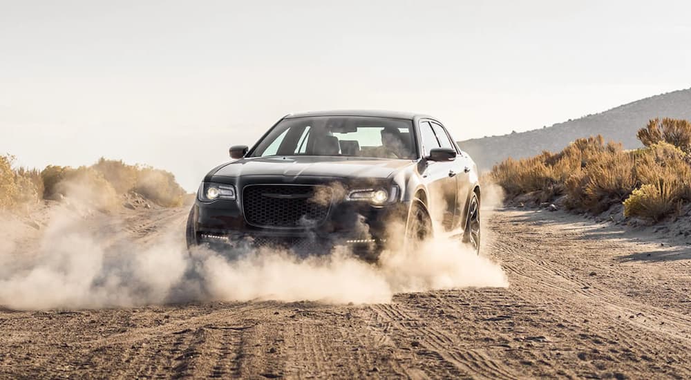A black 2021 Chrysler 300 is shown doing a burn out on a dusty dirt road.