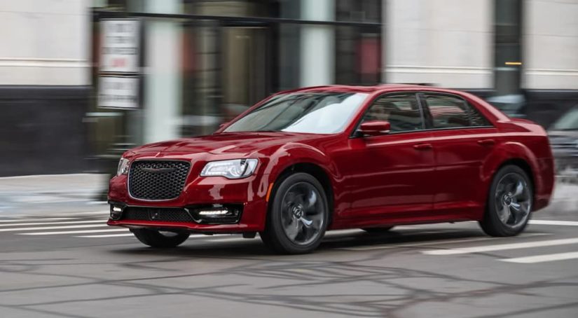 A red 2021 Chrysler 300 is shown from the side driving through a city.