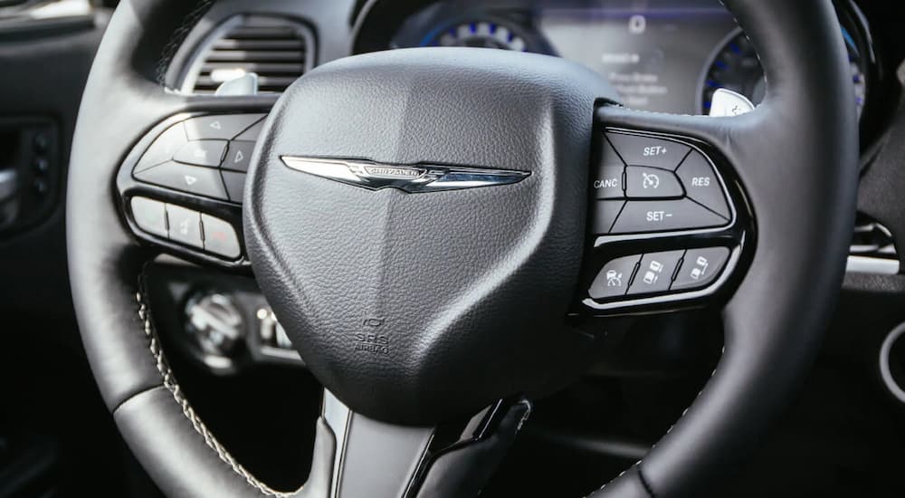 The black interior of a 2021 Chrysler 300 shows the steering wheel.