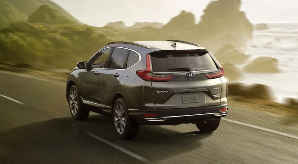 A grey 2021 Nissan Rogue Hybrid Touring is shown from the rear past a lake.