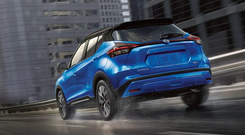 A blue 2021 Nissan Kicks is shown from the rear driving through a city.