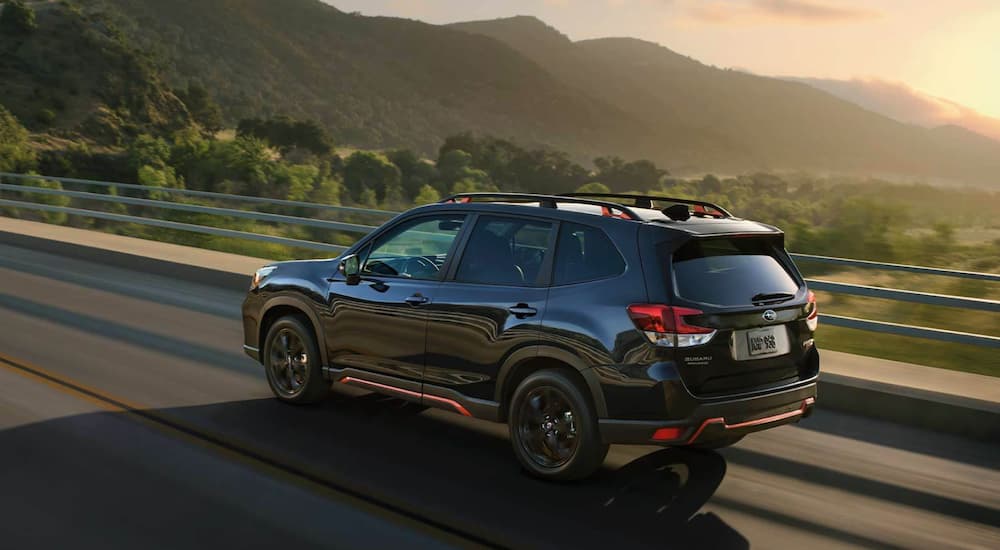 A black 2021 Subaru Forester Sport is shown driving on an open road at sunset.