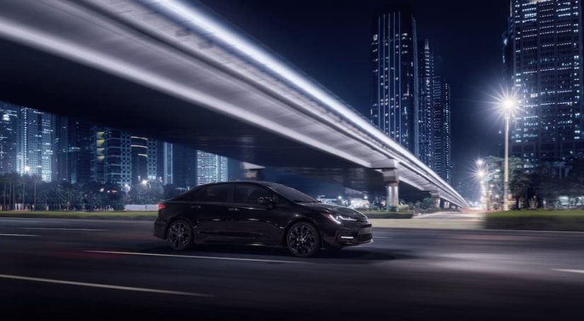 A black 2021 Toyota Corolla SE Nightshade Edition is shown driving under a bridge at night.
