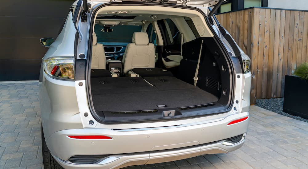 The rear of a 2022 Buick Enclave is show with an open lift-gate parked in a modern driveway.