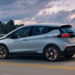 A blue 2022 Chevy Bolt EV is shown from the side driving over a bridge at sunset.