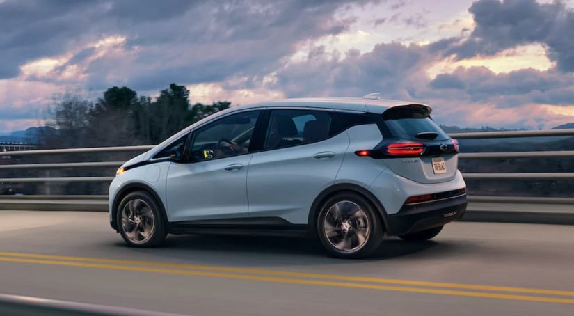 A blue 2022 Chevy Bolt EV is shown from the side driving over a bridge at sunset.