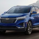 A blue 2022 Chevy Equinox is shown from the front driving past a mountain range.