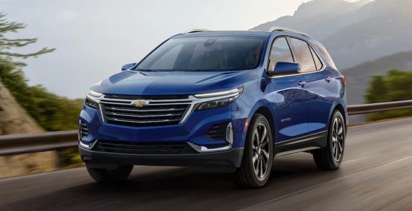 A blue 2022 Chevy Equinox is shown from the front driving past a mountain range.