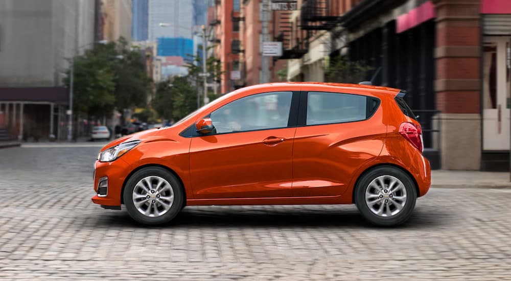 An orange 2022 Chevy Spark is shown from the side driving through a city.