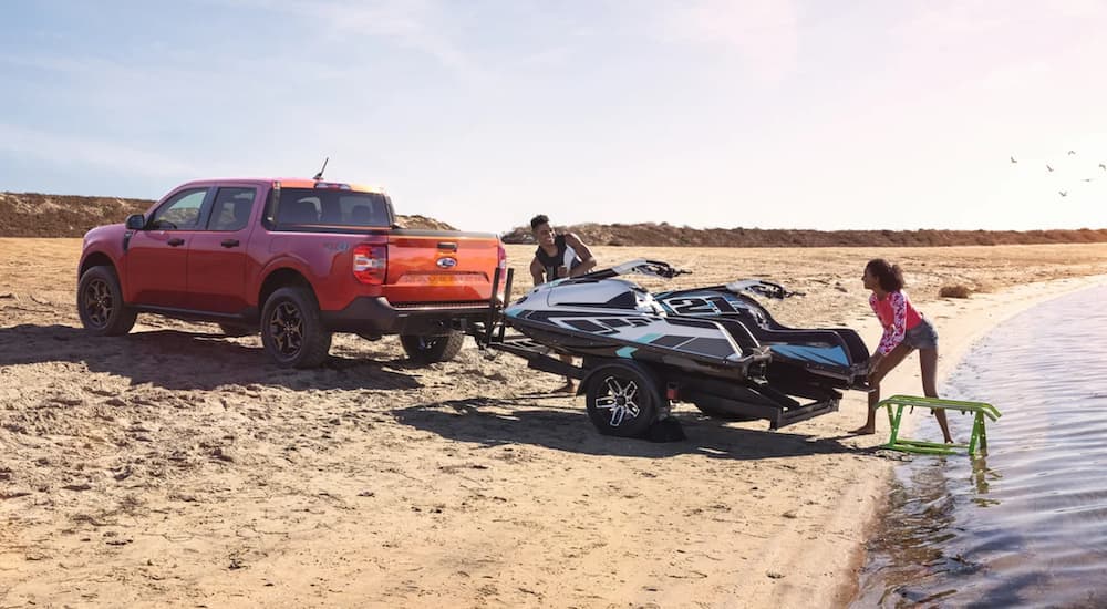 An orange 2022 Ford Maverick is shown towing a jet-ski next to the ocean.