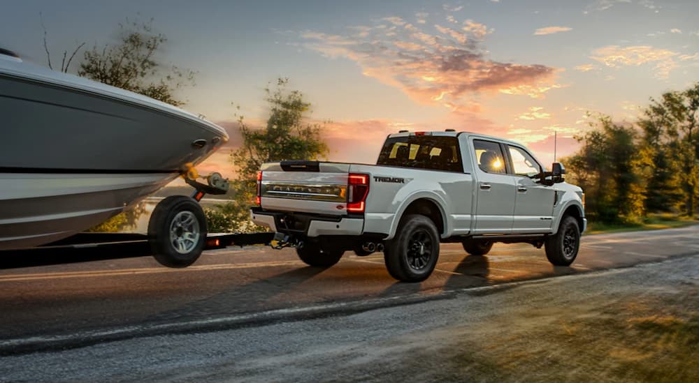 A white 2022 Ford Super Duty Tremor is shown towing a boat on an open road at sunset.