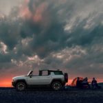 A white 2024 GMC Hummer EV SUV is shown from the side at sunset.