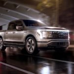 A silver 2022 Ford F-150 Lightning is shown from the side driving through the city.