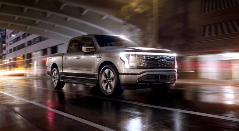 A silver 2022 Ford F-150 Lightning is shown from the side driving through the city.