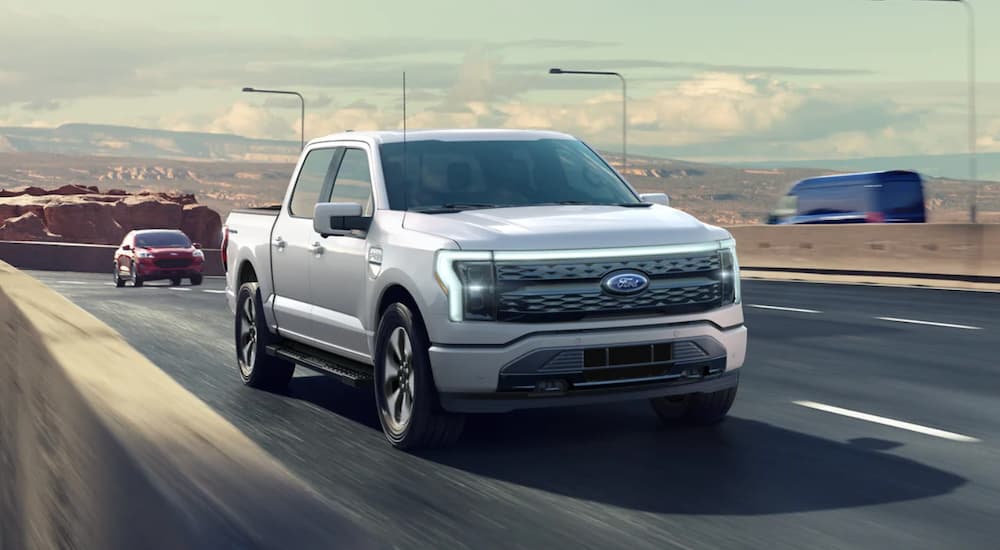 A white 2022 Ford F-150 Lightning is shown from the front driving on a highway.