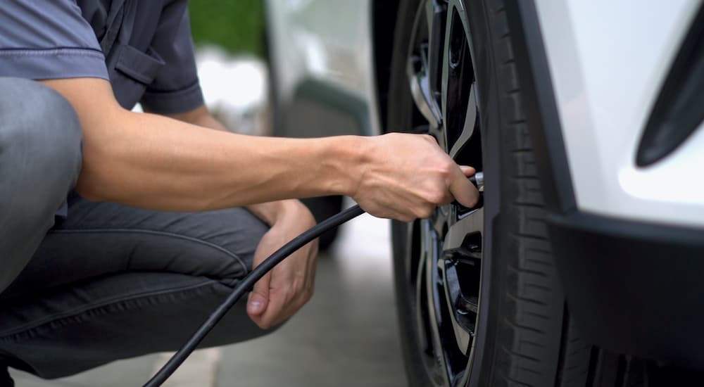 A man is shown filling a tire with air after searching for a used car for sale near you.