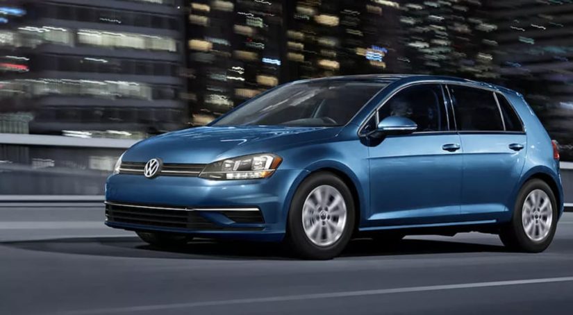 A blue 2021 Volkswagen Golf is shown driving in a city at night after leaving a Volkswagen dealership.