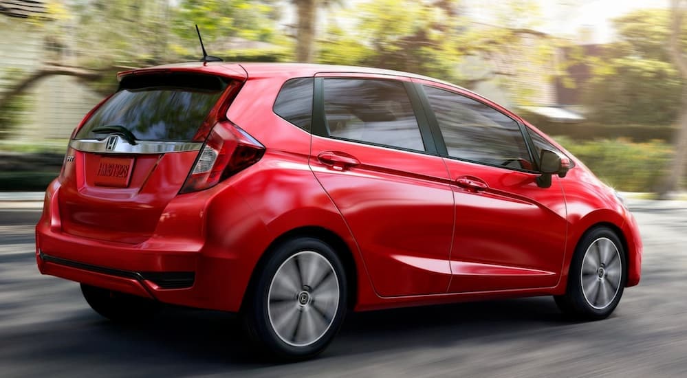 A red 2020 Honda Fit is shown from the side driving away from a used car dealer.