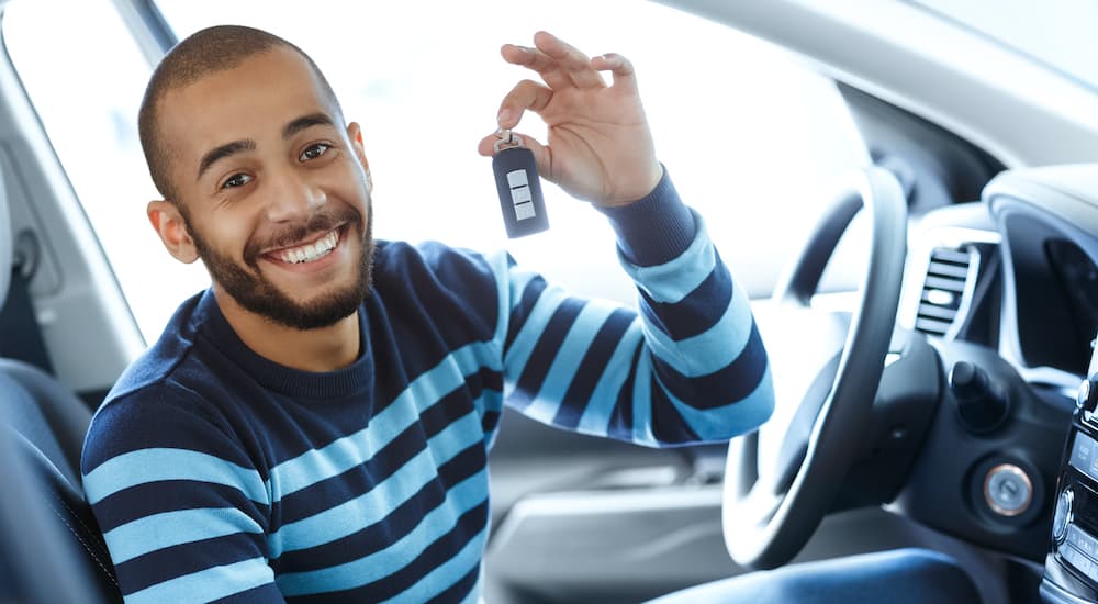 A man is holding a set of car keys while sitting in the front seat of a car.