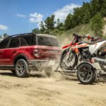 A red 2021 Ford Bronco Sport Outer Banks is shown towing dirt bikes over dirt.