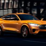 A yellow 2021 Ford Mustang Mach-E is shown driving through a city at night after winning a 2021 Ford Mustang Mach-E vs. 2021 Tesla Model Y comparison.