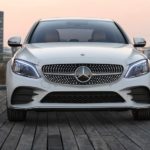 A white 2021 Mercedes C-Class is shown from the front with a city landscape.
