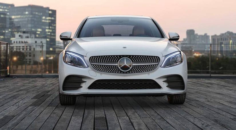A white 2021 Mercedes C-Class is shown from the front with a city landscape.