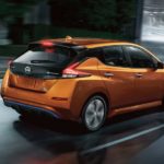 An orange 2021 Nissan LEAF is shown from the side driving through a city at night.