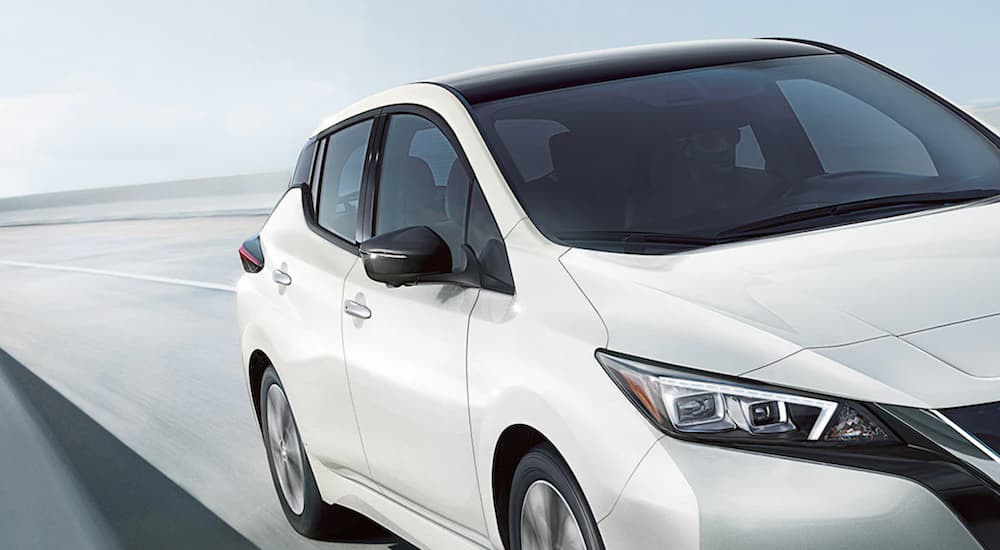 A white 2021 Nissan LEAF is show in close up driving on an open road.