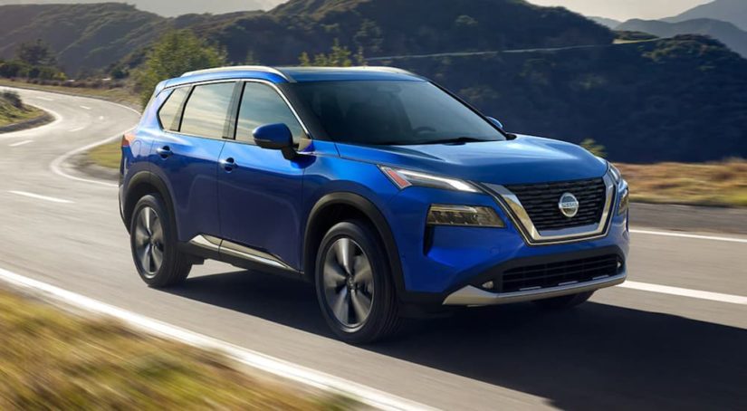 A blue 2021 Nissan Rogue is shown from the side driving on an open road after winning a 2021 Nissan Rogue vs 2021 Toyota RAV4 comparison.