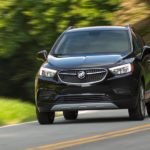A black 2022 Buick Encore is shown driving down a road with trees in the background.