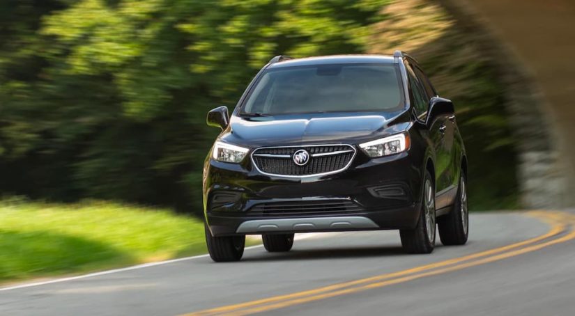 A black 2022 Buick Encore is shown driving down a road with trees in the background.