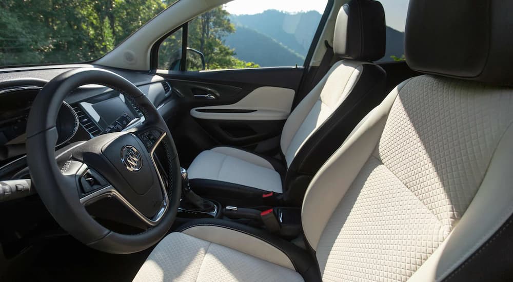 The white and black interior of a 2022 Buick Encore shows the steering wheel and front seat.