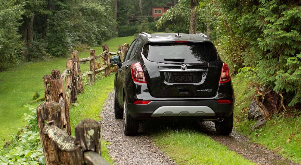 A black 2022 Buick Encore is shown from the rear driving on a dirt road in the forest.