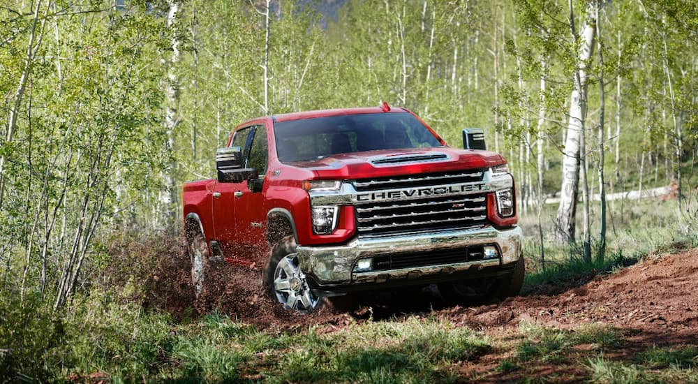 A red 2022 Chevy Silverado 2500HD is shown driving on dirt path in a forest.
