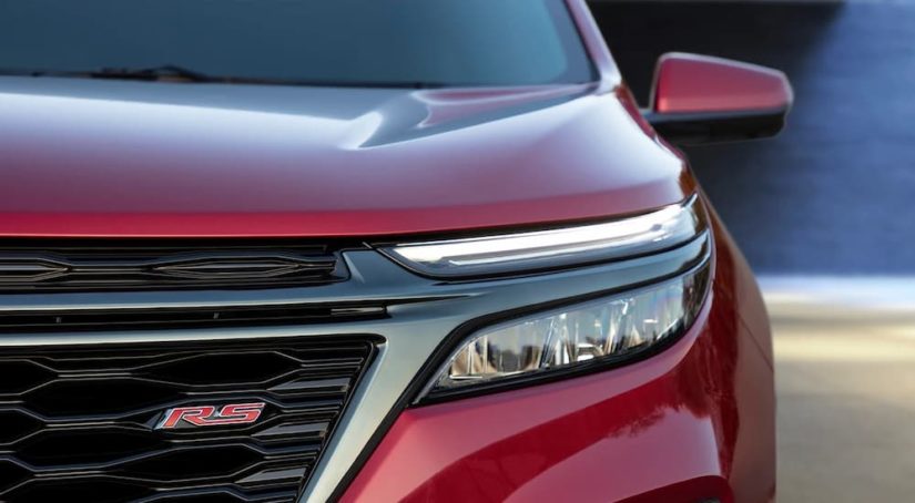 The driver side headlight and grille are shown on a red 2022 Chevy Equinox RS.