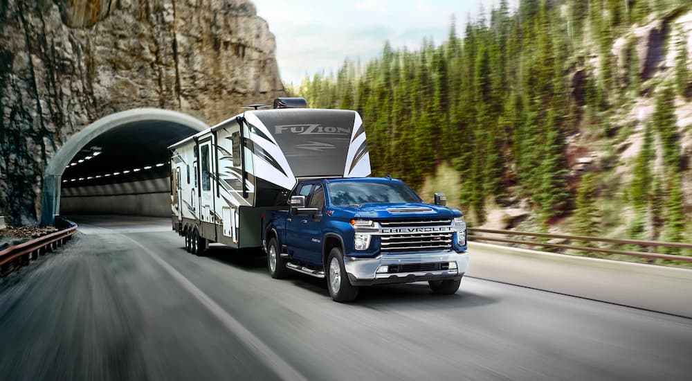 A blue 2022 Chevy Silverado 2500HD is shown towing a fifth wheel camper on a mountain highway.