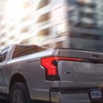 A grey 2022 Ford F-150 Lightning Lariat is shown from behind driving through a city.
