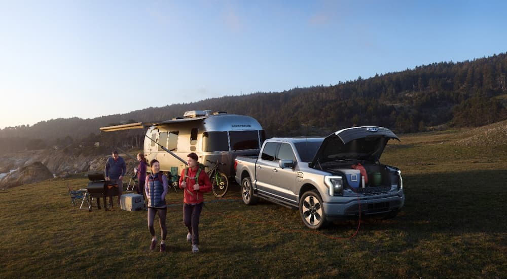 A grey 2022 Ford F-150 Lightning Platinum is shown hitched to an airstream at an oceanside campsite.
