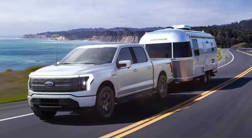 A silver 2022 Ford F-150 Lightning is shown towing an airstream by the ocean after a 2022 Ford F-150 Lightning vs 2022 Rivian R1T comparison.