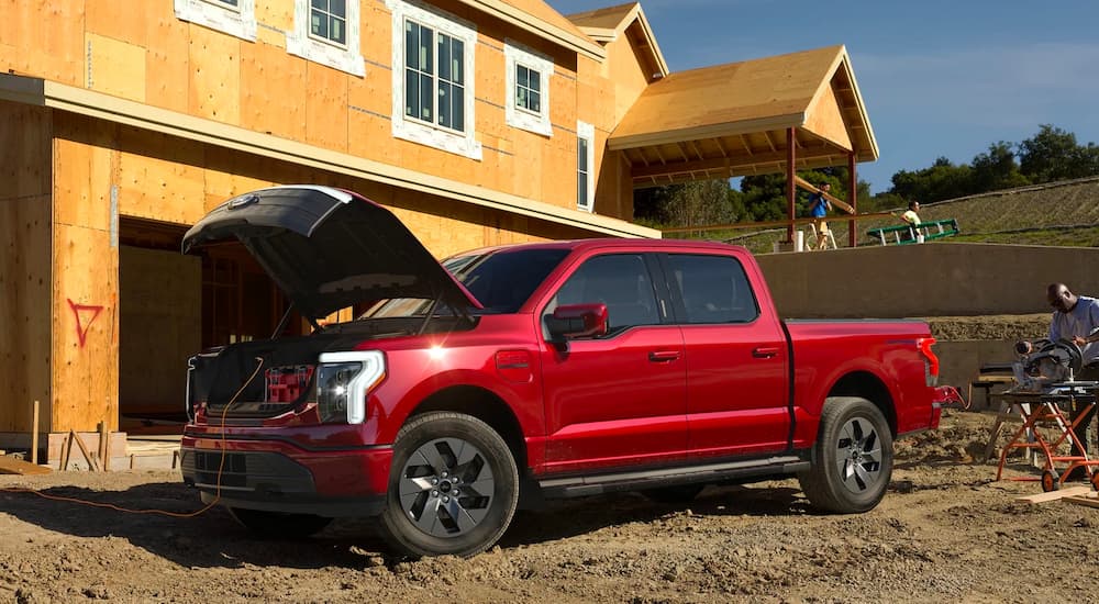 A side view of a red 2022 Ford F-150 Lightning is shown at a construction site.