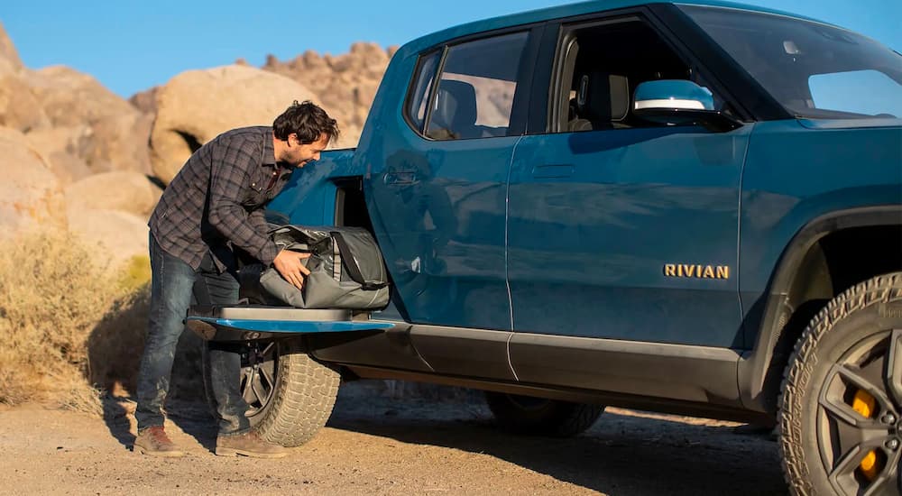 A man is shown storing camping gear in a blue 2022 Rivian R1T.